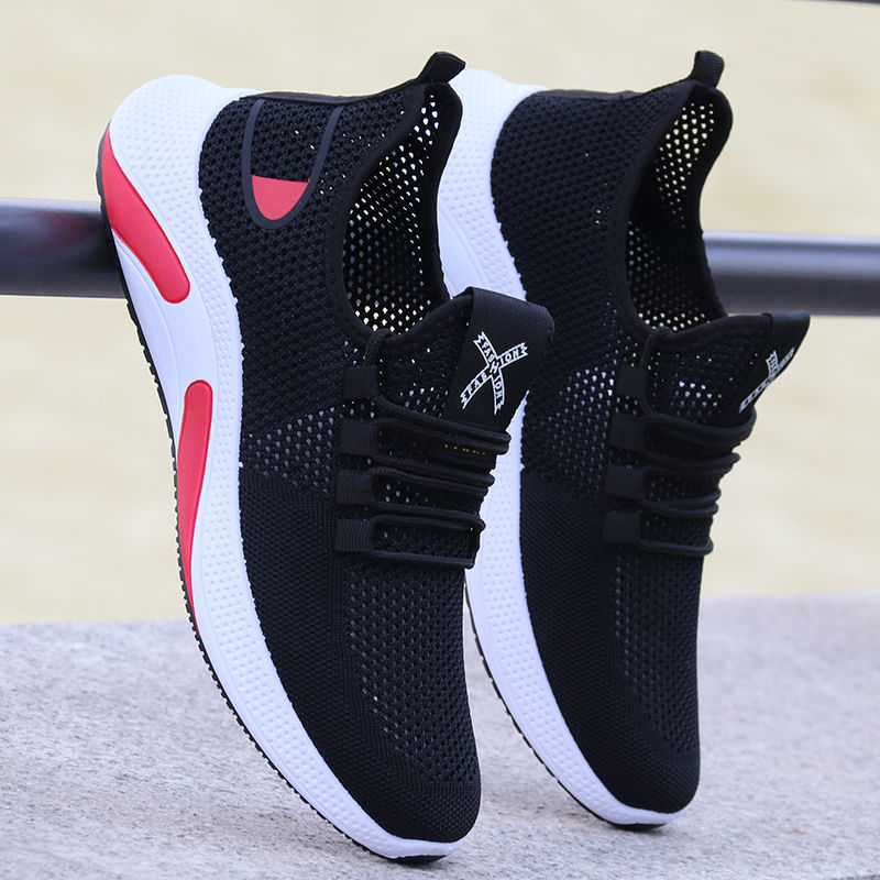 Scarpe da ginnastica nere con suola bianca e dettagli rossi, design traspirante, posizionate su una superficie di cemento. Scarpe sportive moderne.