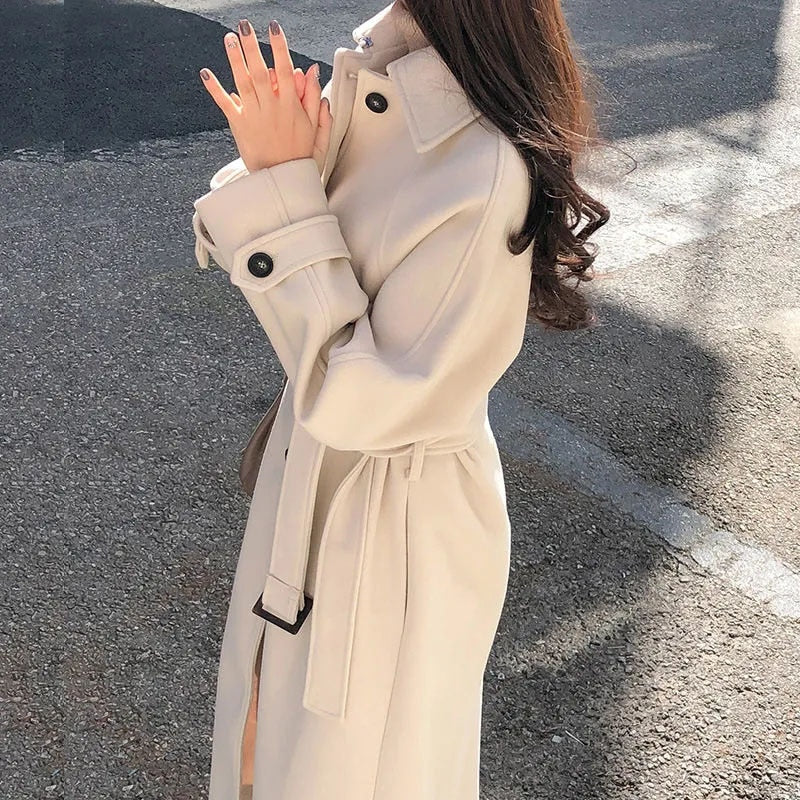 Donna con cappotto beige elegante, cintura in vita, su strada asfaltata. Moda autunnale, stile urbano, abbigliamento femminile chic.