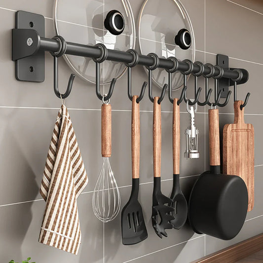 Portautensili da cucina a parete con ganci, utensili in legno e metallo, coperchi pentole, tagliere e strofinaccio a righe. Organizzazione cucina.