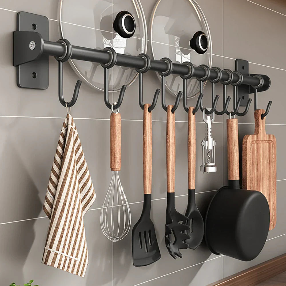 Portautensili da cucina a parete con ganci, utensili in legno e metallo, coperchi pentole, tagliere e strofinaccio a righe. Organizzazione cucina moderna.