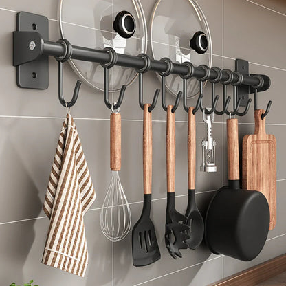 Portautensili da cucina a parete con ganci, utensili in legno e metallo, coperchi pentole, tagliere e strofinaccio a righe. Organizzazione cucina moderna.