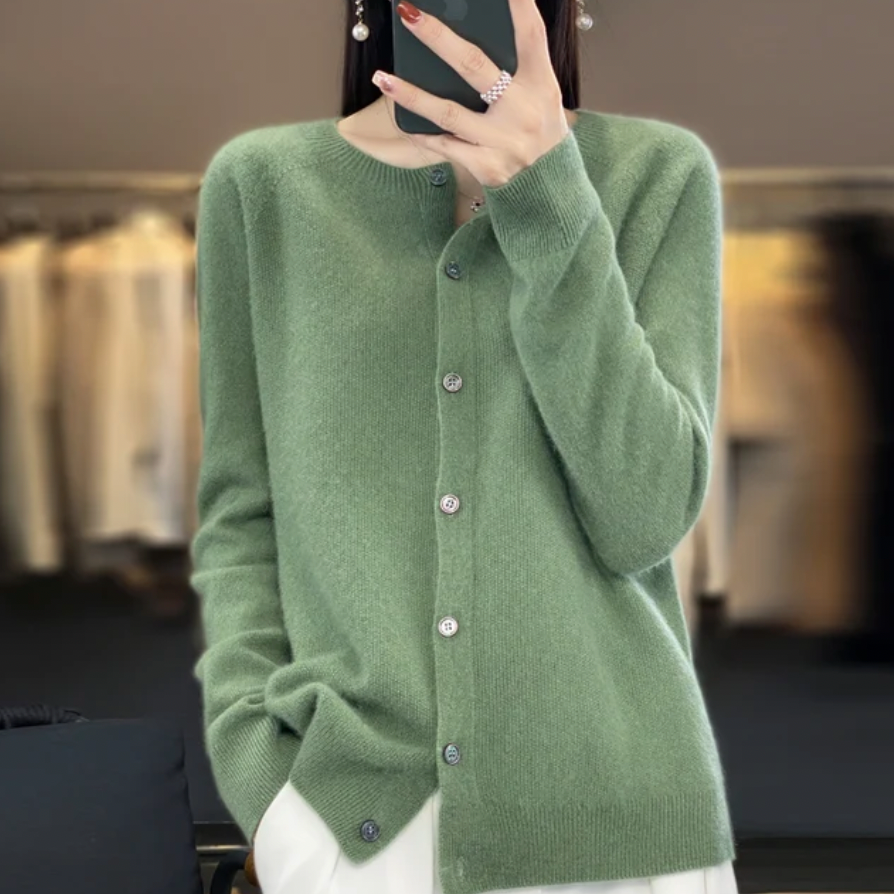 Donna con cardigan verde in cashmere, bottoni frontali, sfondo con abiti sfocati. Moda autunnale, abbigliamento elegante e confortevole.