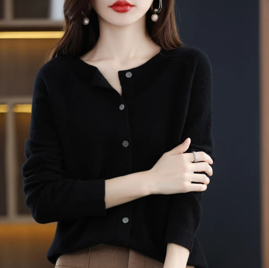 Donna con cardigan nero elegante, orecchini a perla, anello argento, sfondo sfocato. Moda autunnale, stile minimalista, abbigliamento femminile.