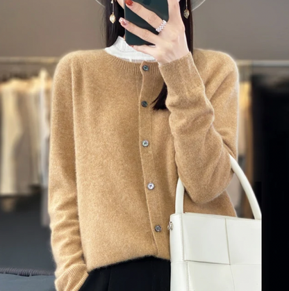 Donna con cardigan beige, cappello grigio e borsa bianca in negozio di moda. Stile autunnale elegante, abbigliamento casual chic.