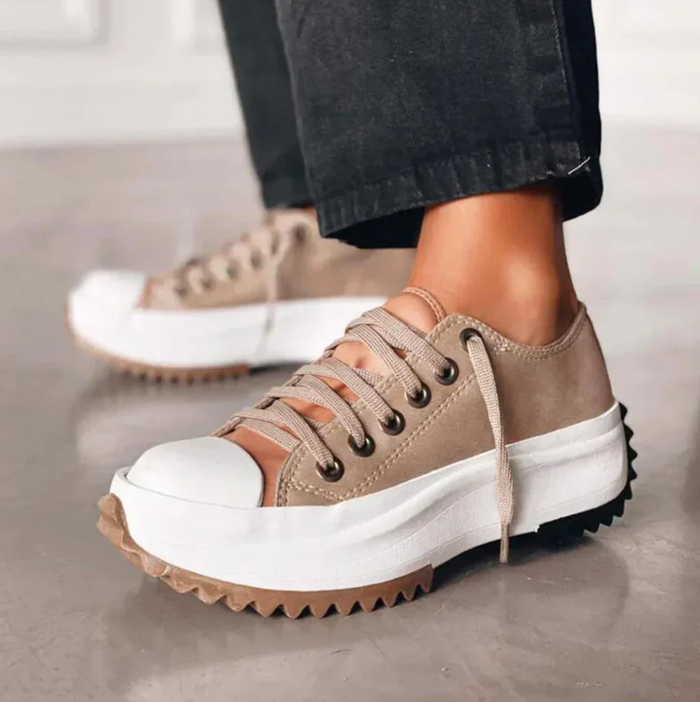 Scarpe da ginnastica beige con suola spessa bianca e marrone, lacci beige, indossate con pantaloni neri. Scarpe moda casual, tendenza 2023.