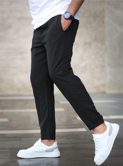 Uomo con pantaloni neri eleganti, scarpe da ginnastica bianche e orologio blu, cammina su marciapiede. Moda casual maschile, stile urbano.