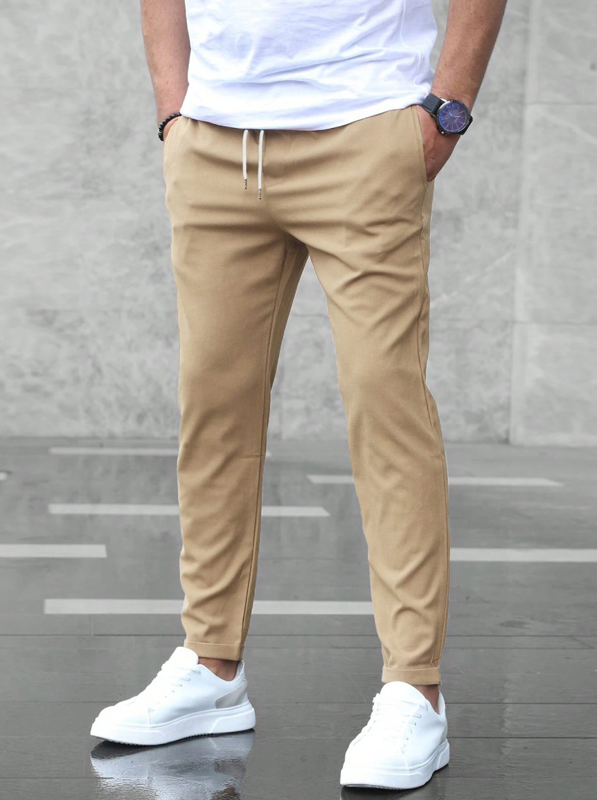 Uomo con pantaloni chino beige, t-shirt bianca e scarpe da ginnastica bianche. Look casual ed elegante, moda maschile contemporanea.