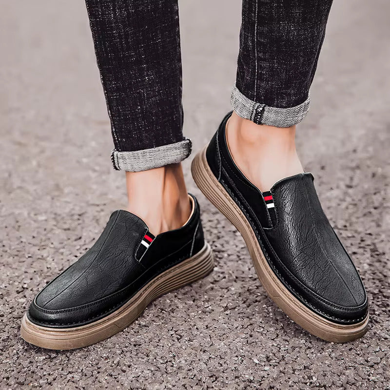 Scarpe slip-on nere da uomo, suola marrone, dettagli rossi e bianchi, indossate con jeans scuri. Calzature eleganti e casual per ogni occasione.