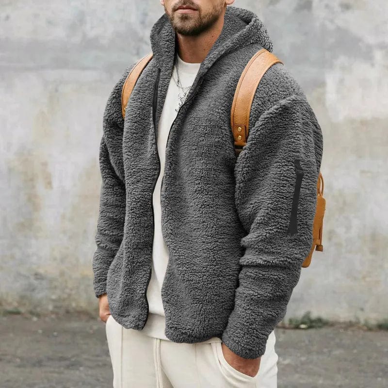 Uomo con giacca in pile grigio, zaino marrone, sfondo urbano. Moda invernale, abbigliamento casual, stile moderno.