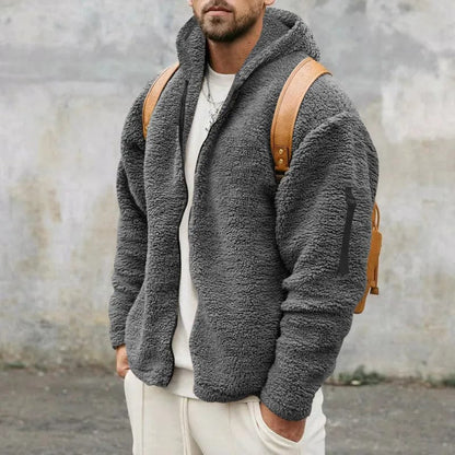 Uomo con giacca in pile grigio, zaino marrone, sfondo urbano. Moda invernale, abbigliamento casual, stile moderno.
