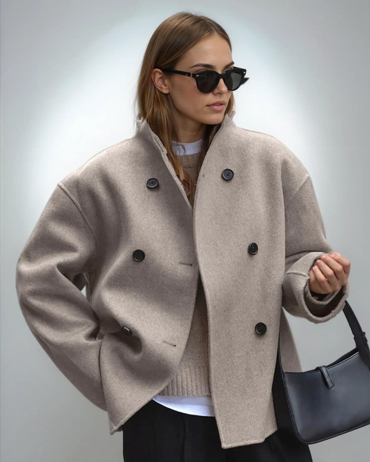 Donna con cappotto beige oversize, occhiali da sole neri e borsa a tracolla nera. Moda autunnale elegante e moderna.