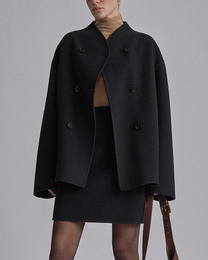 Donna con cappotto nero oversize, doppio petto, abbinato a gonna nera e dolcevita beige. Moda autunno inverno, stile elegante e minimalista.