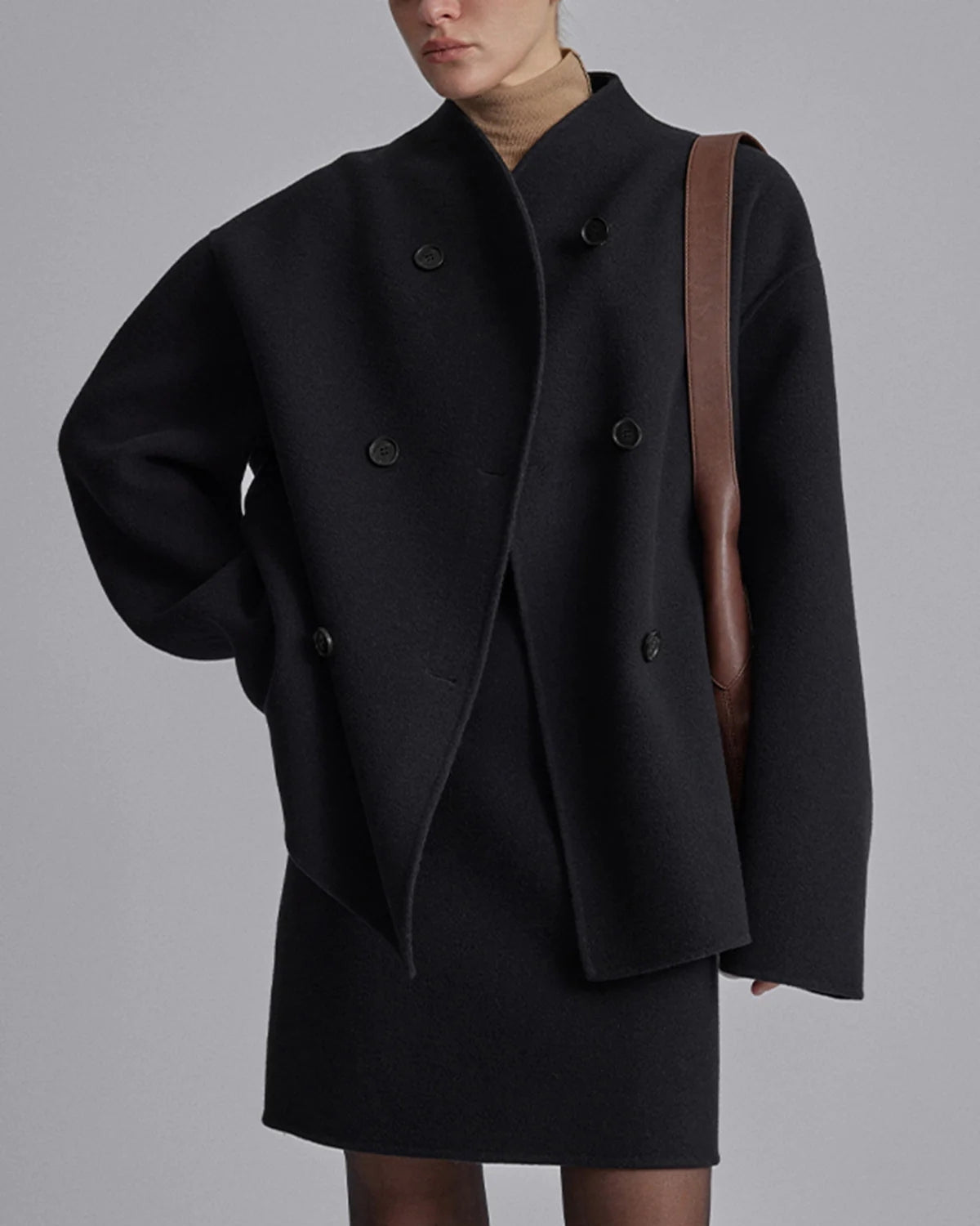 Donna con cappotto nero oversize, doppio petto, elegante e moderno, abbinato a borsa marrone. Moda autunnale, stile minimalista.