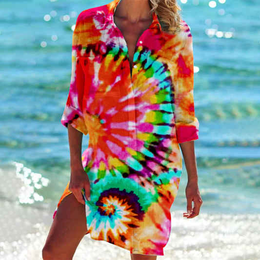 Donna in abito estivo tie-dye colorato sulla spiaggia, mare azzurro sullo sfondo. Moda estiva, abbigliamento casual, tendenze 2023.