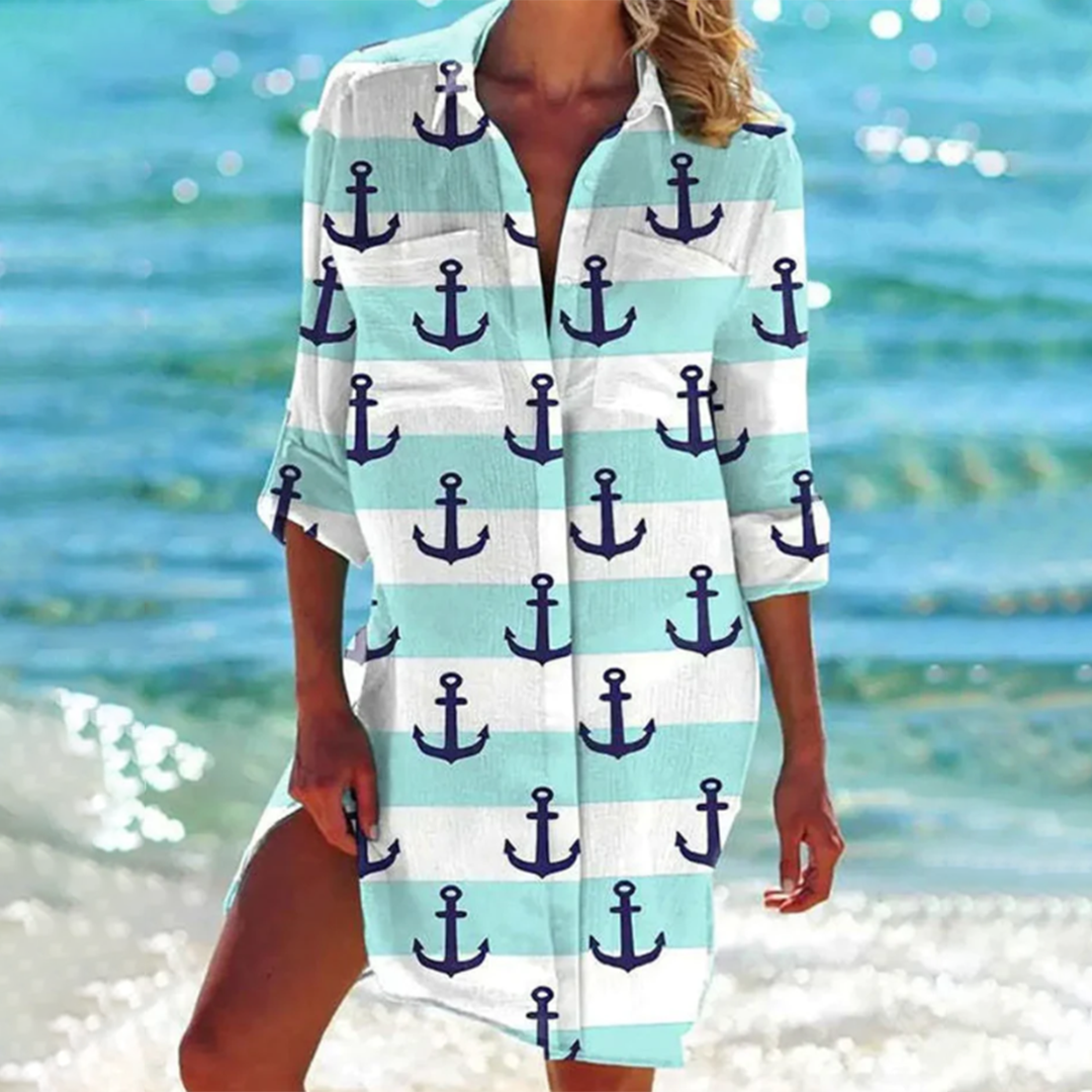 Donna in spiaggia con copricostume a righe bianche e azzurre, decorato con ancore blu. Moda estiva, abbigliamento mare, stile nautico.