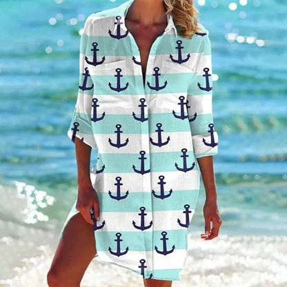 Donna in spiaggia con copricostume a righe bianche e azzurre, decorato con ancore blu. Moda estiva, abbigliamento mare, stile nautico.