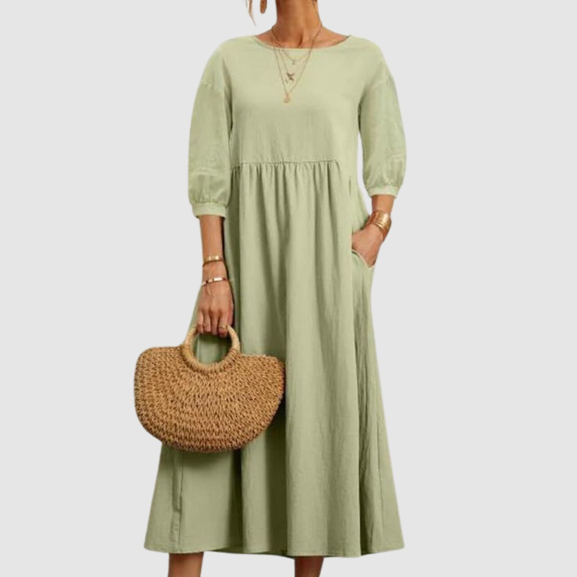 Abito lungo verde salvia con maniche a tre quarti, indossato con borsa in paglia intrecciata. Stile casual elegante, moda donna primavera estate.
