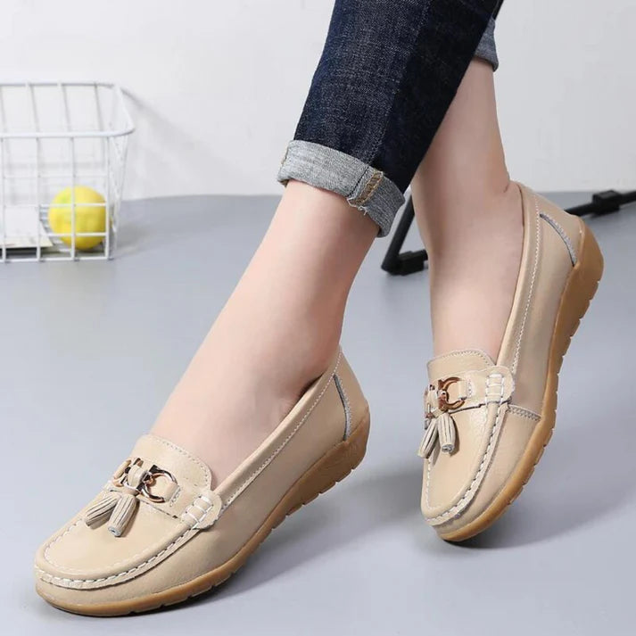Scarpe mocassini beige da donna con nappine, suola in gomma antiscivolo, indossate con jeans. Calzature eleganti e comode per uso quotidiano.