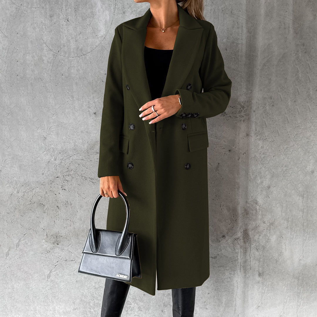 Donna con cappotto lungo verde scuro, borsa nera elegante, sfondo grigio. Moda autunnale, stile sofisticato, abbigliamento femminile di tendenza.