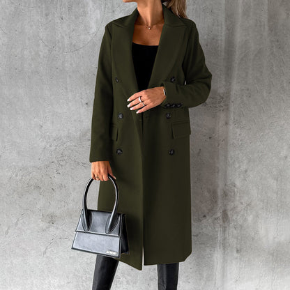 Donna con cappotto lungo verde scuro, borsa nera elegante, sfondo grigio. Moda autunnale, stile sofisticato, abbigliamento femminile di tendenza.