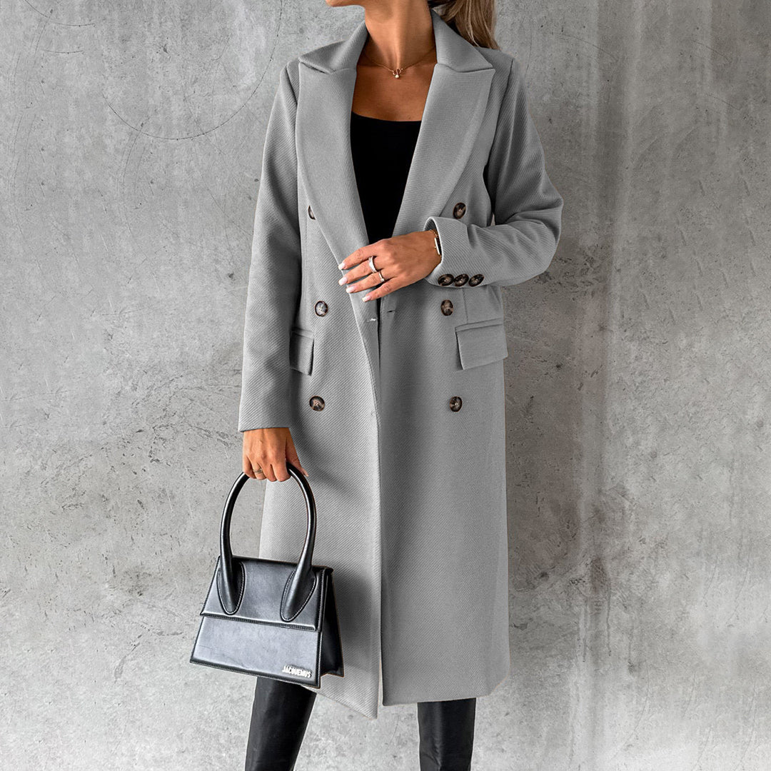 Donna con cappotto grigio elegante, borsa nera, sfondo grigio. Moda autunnale, stile sofisticato, abbigliamento femminile di tendenza.