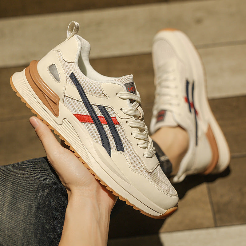 Scarpe da ginnastica bianche con dettagli blu e rossi, suola in gomma marrone, indossate su pavimento in legno. Design moderno e sportivo.