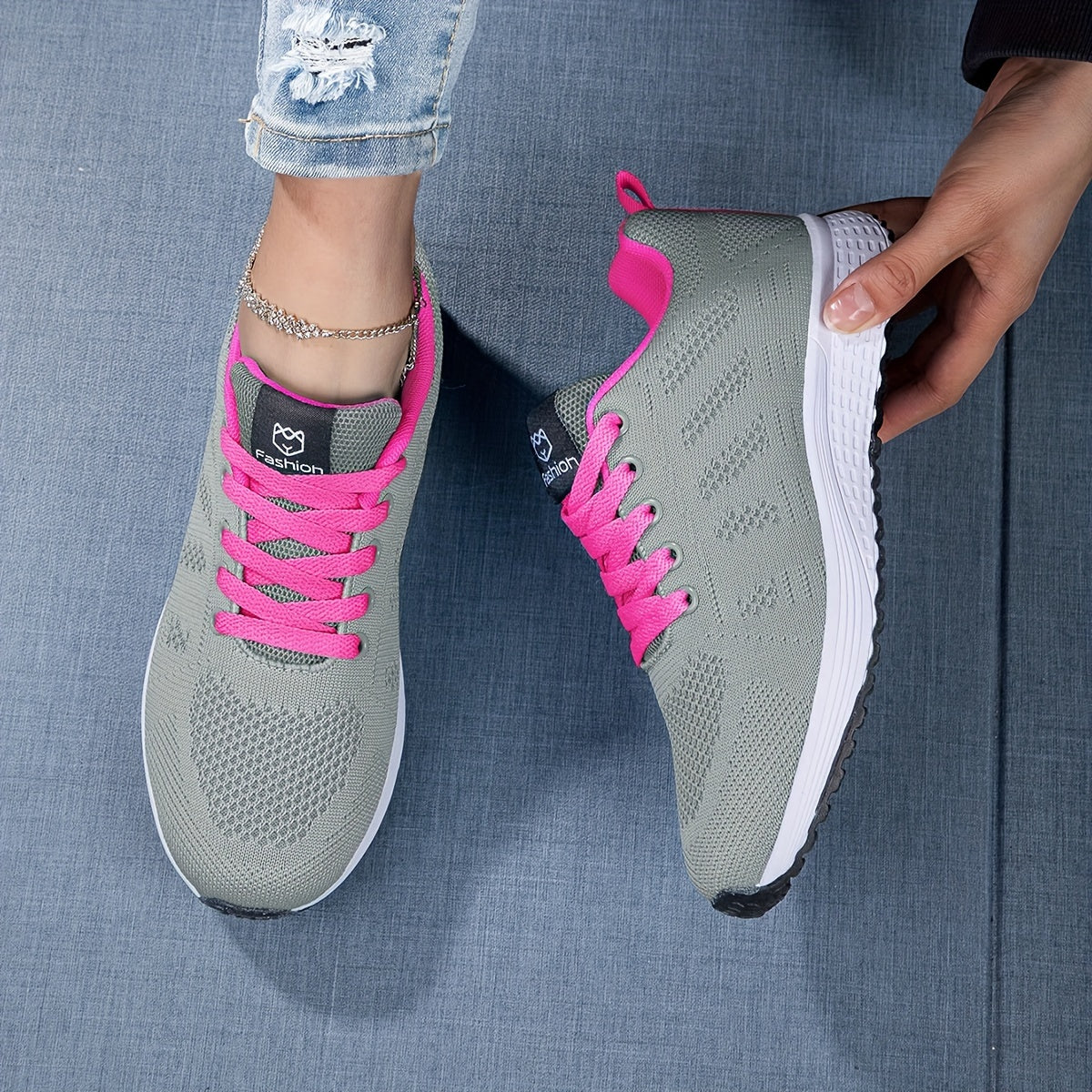Scarpe da ginnastica grigie con lacci rosa su sfondo blu, indossate da una persona con jeans strappati. Scarpe sportive moda donna, comode e trendy.