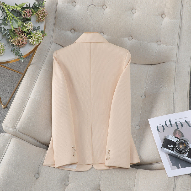 Giacca beige elegante su divano beige, accanto a rivista di moda e fotocamera vintage. Stile moderno, abbigliamento formale, arredamento chic.