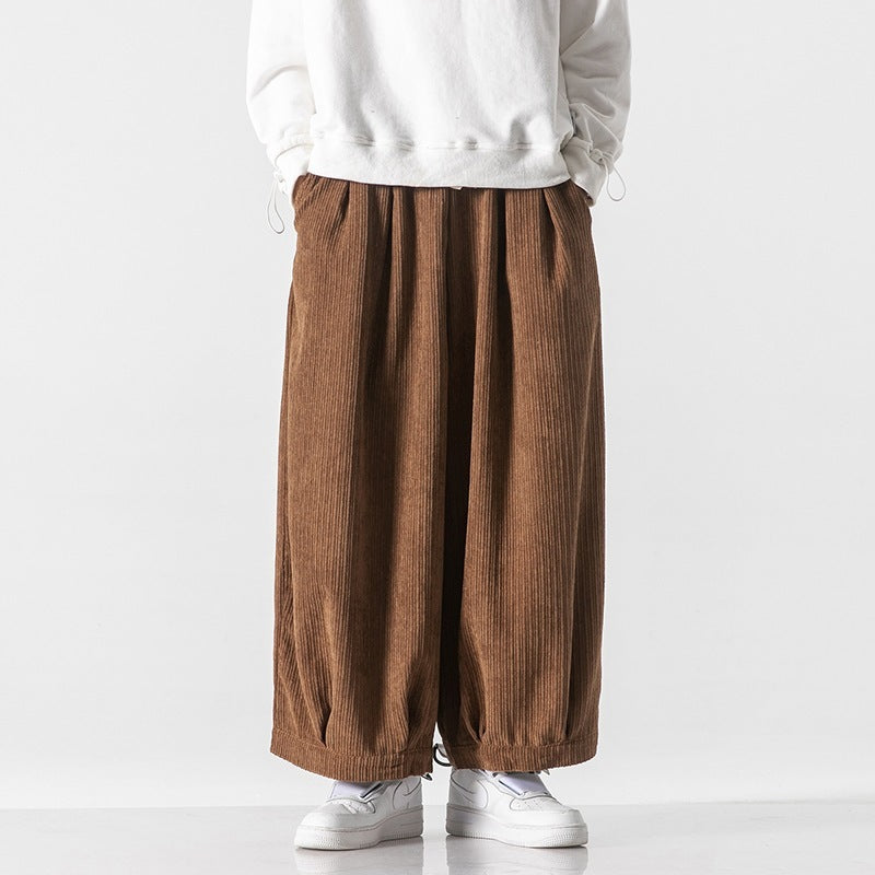 Pantaloni larghi marroni in velluto a coste, indossati con felpa bianca e sneakers bianche. Moda casual uomo, stile autunnale.