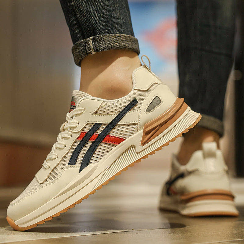 Scarpe da ginnastica bianche con dettagli blu e rossi, suola in gomma marrone, indossate da una persona su pavimento in legno. Moda casual uomo.