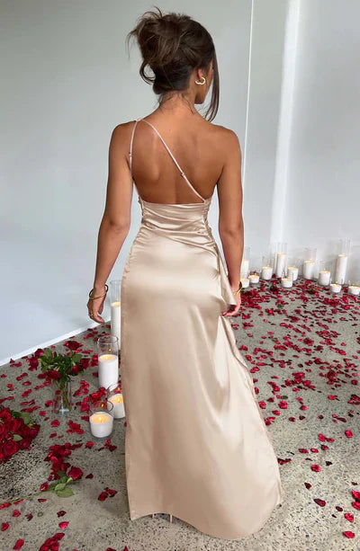 Donna in abito da sera lungo color champagne, schiena scoperta, circondata da petali di rosa rossi e candele bianche su pavimento grigio.