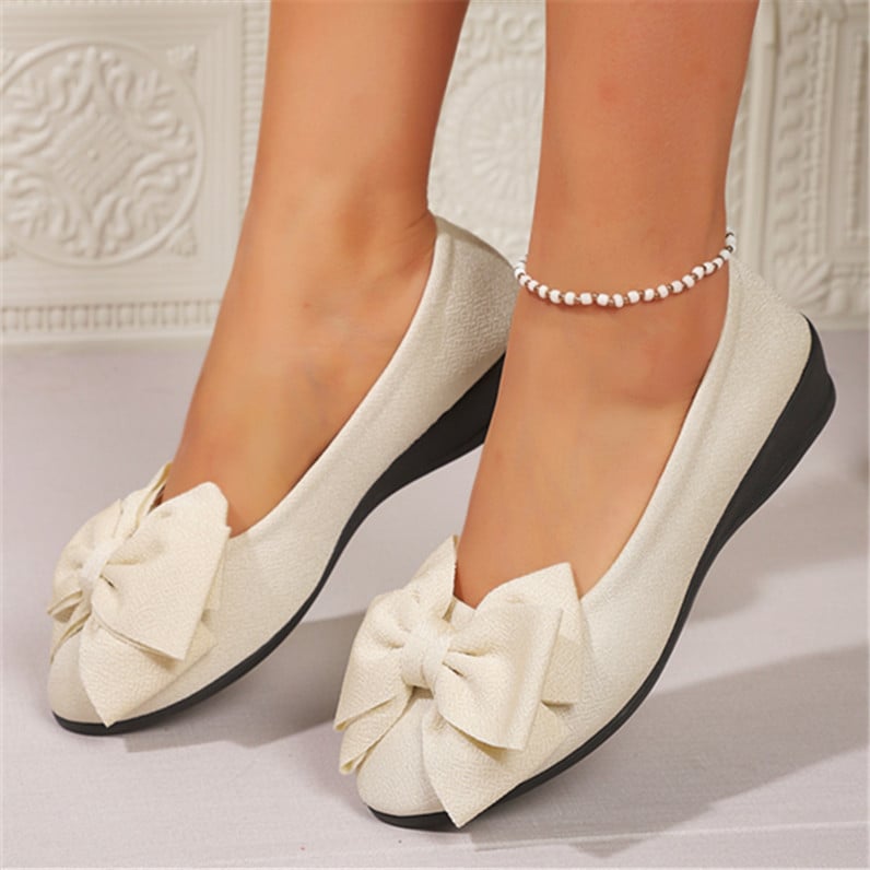 Scarpe ballerine bianche eleganti con fiocco grande, suola nera, indossate con cavigliera di perle. Design raffinato per moda femminile.
