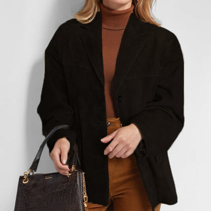 Donna con cappotto nero elegante, maglione marrone e pantaloni ocra, tiene una borsa in pelle nera. Moda autunnale, stile casual chic.