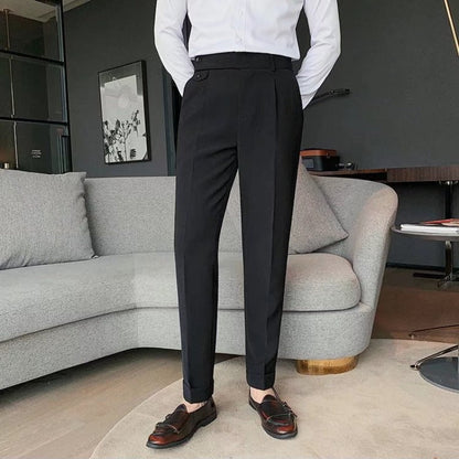 Uomo in pantaloni eleganti neri e camicia bianca, in piedi accanto a un divano grigio in un salotto moderno. Scarpe in pelle marrone.