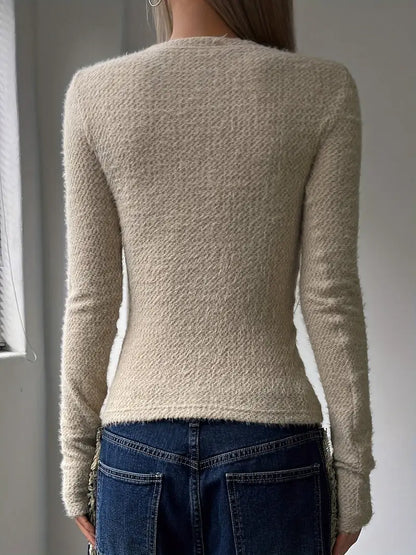 Donna di spalle con maglione beige in lana e jeans blu, in una stanza luminosa. Moda autunnale, abbigliamento casual elegante.