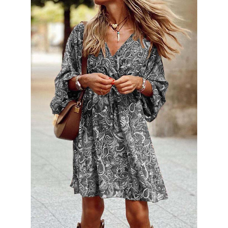 Donna con abito estivo a fantasia floreale, borsa a tracolla marrone, collana e bracciali, cammina in strada. Moda femminile casual elegante.