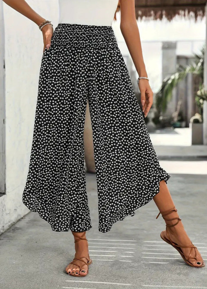 Pantaloni palazzo neri a pois bianchi, indossati con sandali marroni e top bianco. Moda estiva casual, look elegante e comodo.