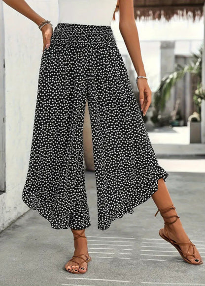 Pantaloni palazzo neri a pois bianchi, indossati con sandali marroni e top bianco. Moda estiva casual, look elegante e comodo.