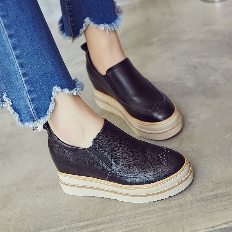 Scarpe slip-on nere in pelle con zeppa, indossate con jeans strappati. Calzature moda donna, comode e casual, ideali per look quotidiani.