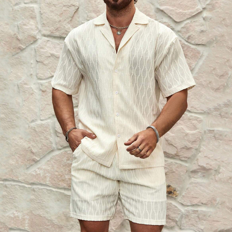 Uomo con completo estivo bianco in lino, camicia a maniche corte e pantaloncini, sfondo di pietra chiara. Moda maschile estiva elegante.