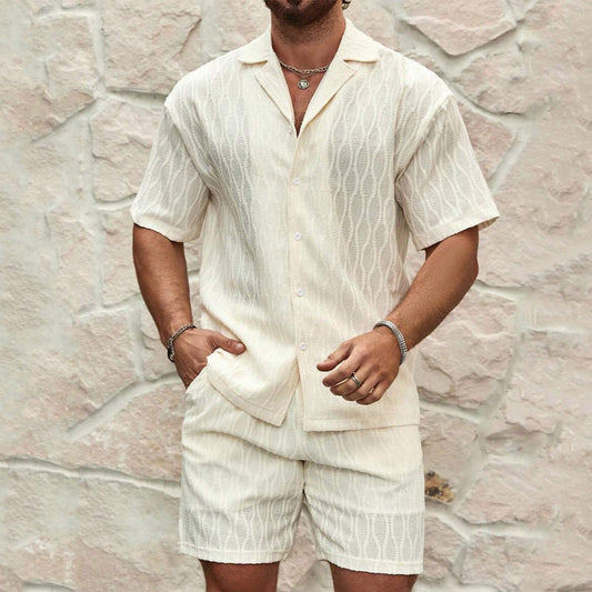 Uomo con completo estivo bianco in lino, camicia a maniche corte e pantaloncini, sfondo di pietra chiara. Moda maschile estiva elegante.
