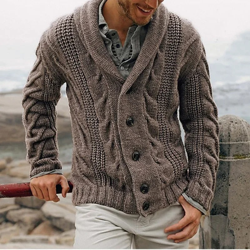 Uomo con cardigan in maglia marrone, bottoni grandi, su sfondo marino. Moda maschile autunnale, stile casual elegante.
