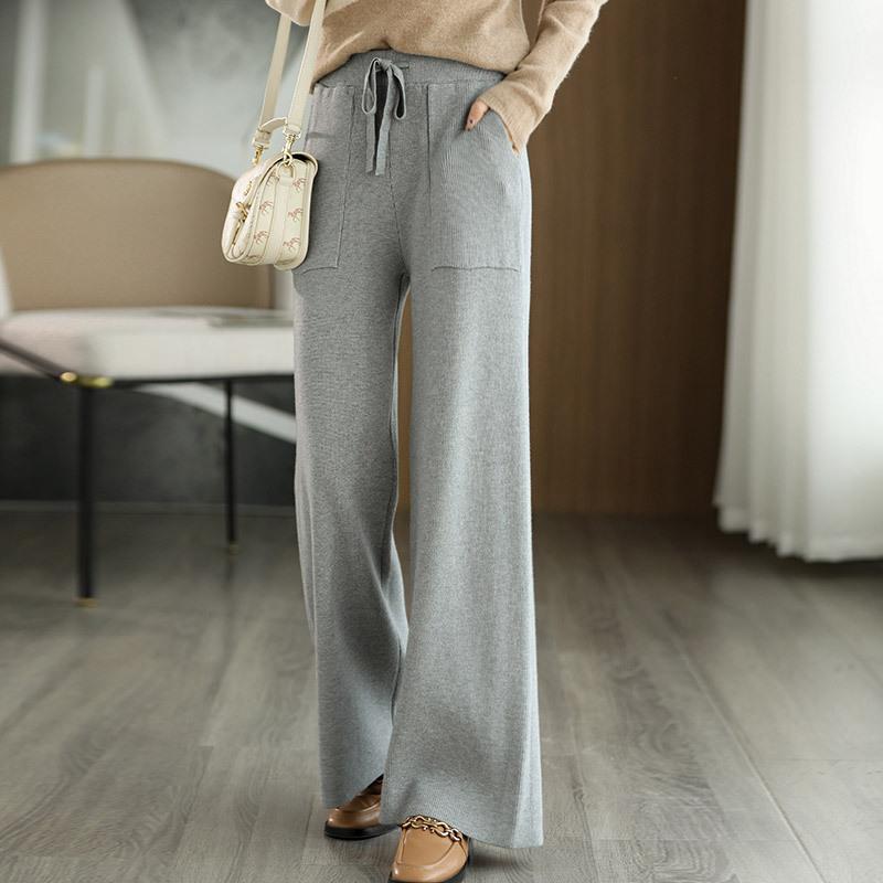 Pantaloni grigi larghi da donna, eleganti e comodi, con tasche e laccio in vita. Moda casual autunnale, abbinati a maglione beige e borsa chiara.