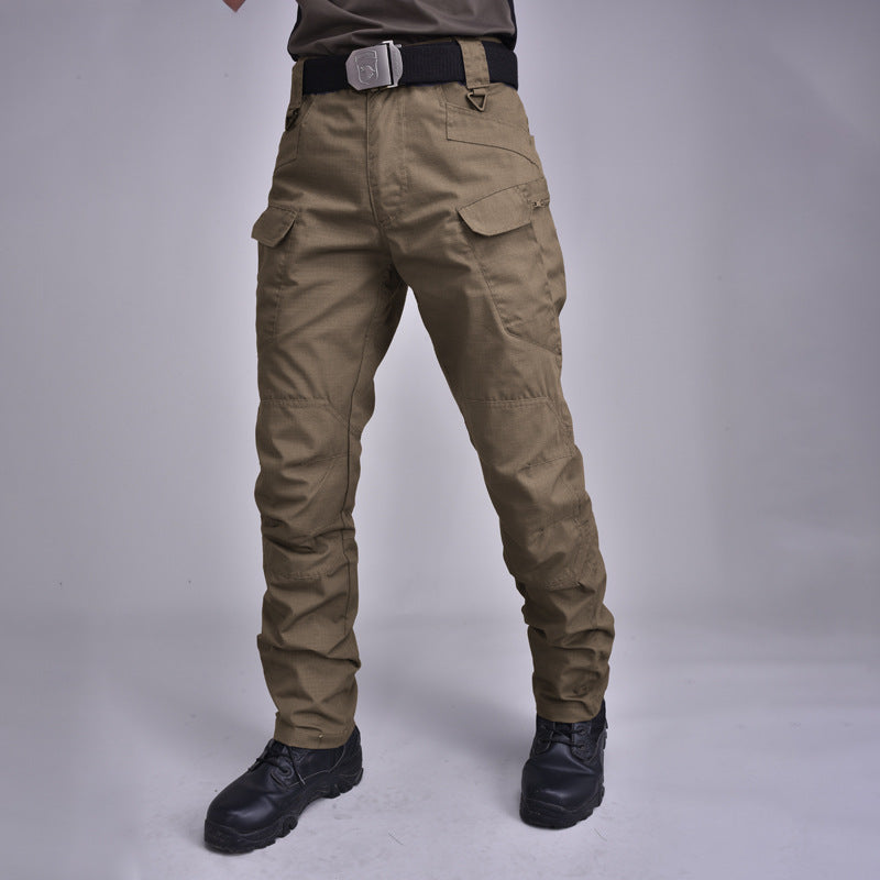 Pantaloni cargo tattici uomo, colore kaki, con tasche multiple e cintura nera, indossati con stivali neri. Abbigliamento outdoor resistente.