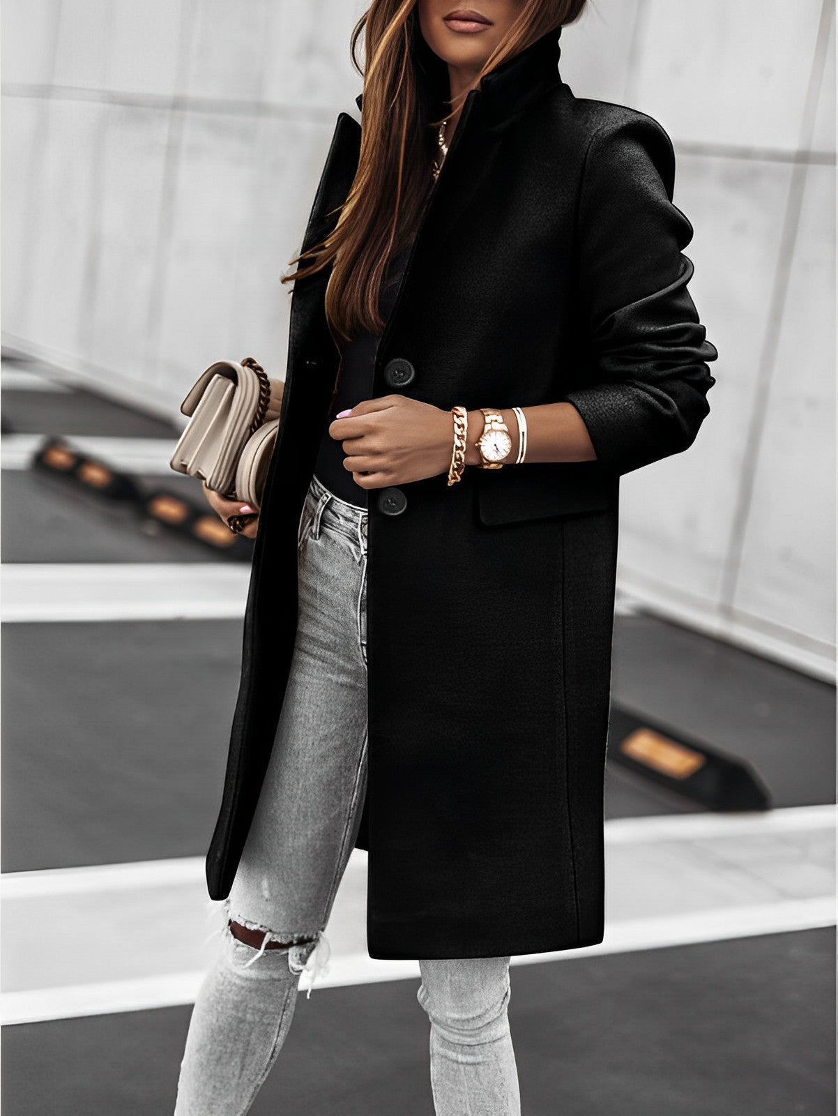Donna con cappotto nero elegante, jeans strappati e accessori dorati, tiene una borsa beige. Moda autunnale, stile urbano chic.