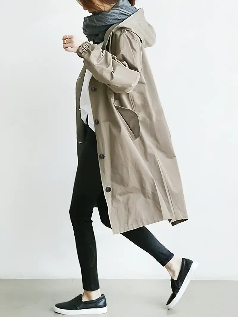 Donna con cappotto beige, sciarpa grigia, pantaloni neri e scarpe slip-on nere. Moda autunnale casual, stile urbano minimalista.