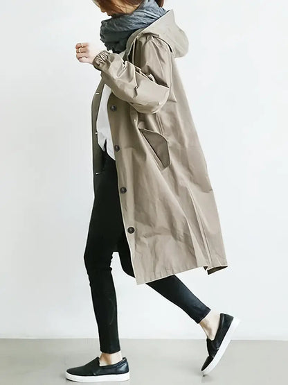 Donna con cappotto beige, sciarpa grigia, pantaloni neri e scarpe slip-on nere. Moda autunnale casual, stile urbano minimalista.