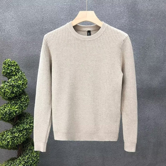 Maglione beige in lana a trama grossa su appendiabiti, sfondo grigio. Elegante e caldo, ideale per moda autunnale e invernale.