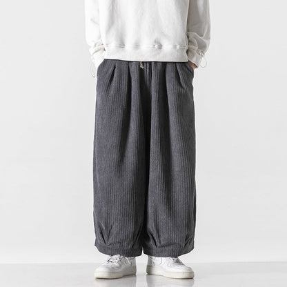Pantaloni larghi grigi a coste, indossati con felpa bianca e scarpe da ginnastica bianche. Moda casual uomo, stile streetwear moderno.