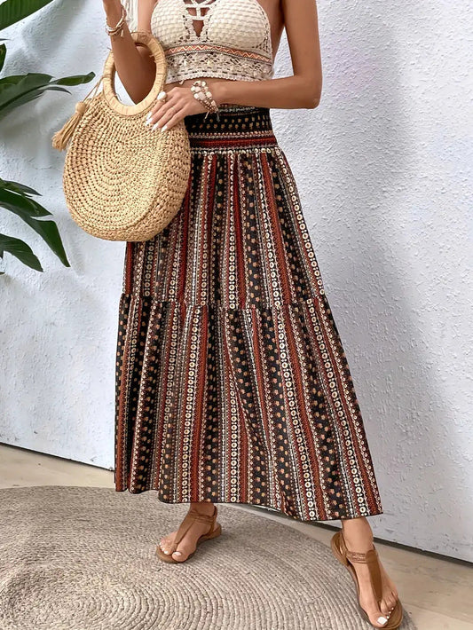Donna con gonna lunga boho a righe etniche e top bianco crochet, borsa di paglia rotonda, sandali marroni. Look estivo casual e chic.